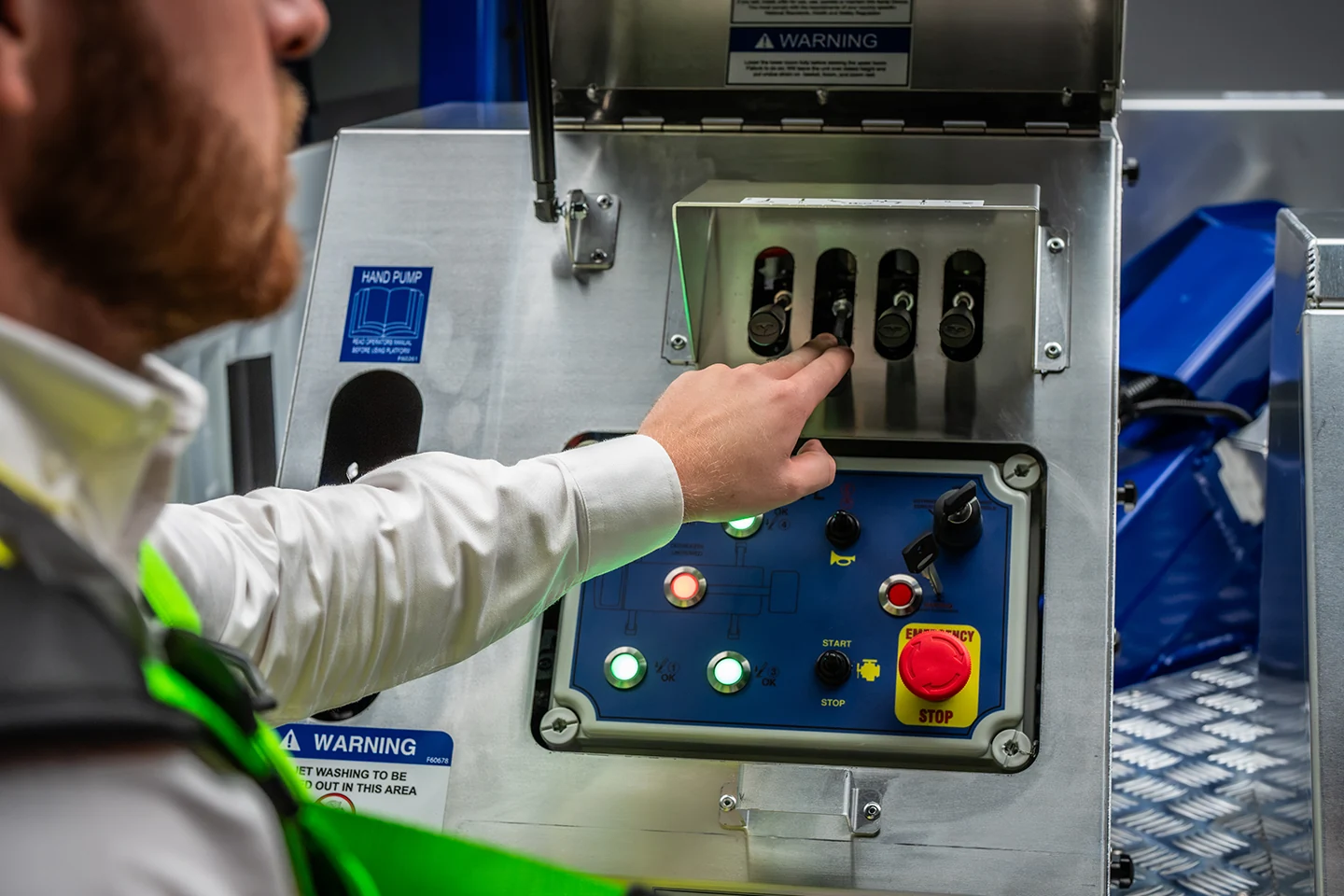 Operator operating the ground controls of a CPL MEWP showing start, stop and emergency stop buttons